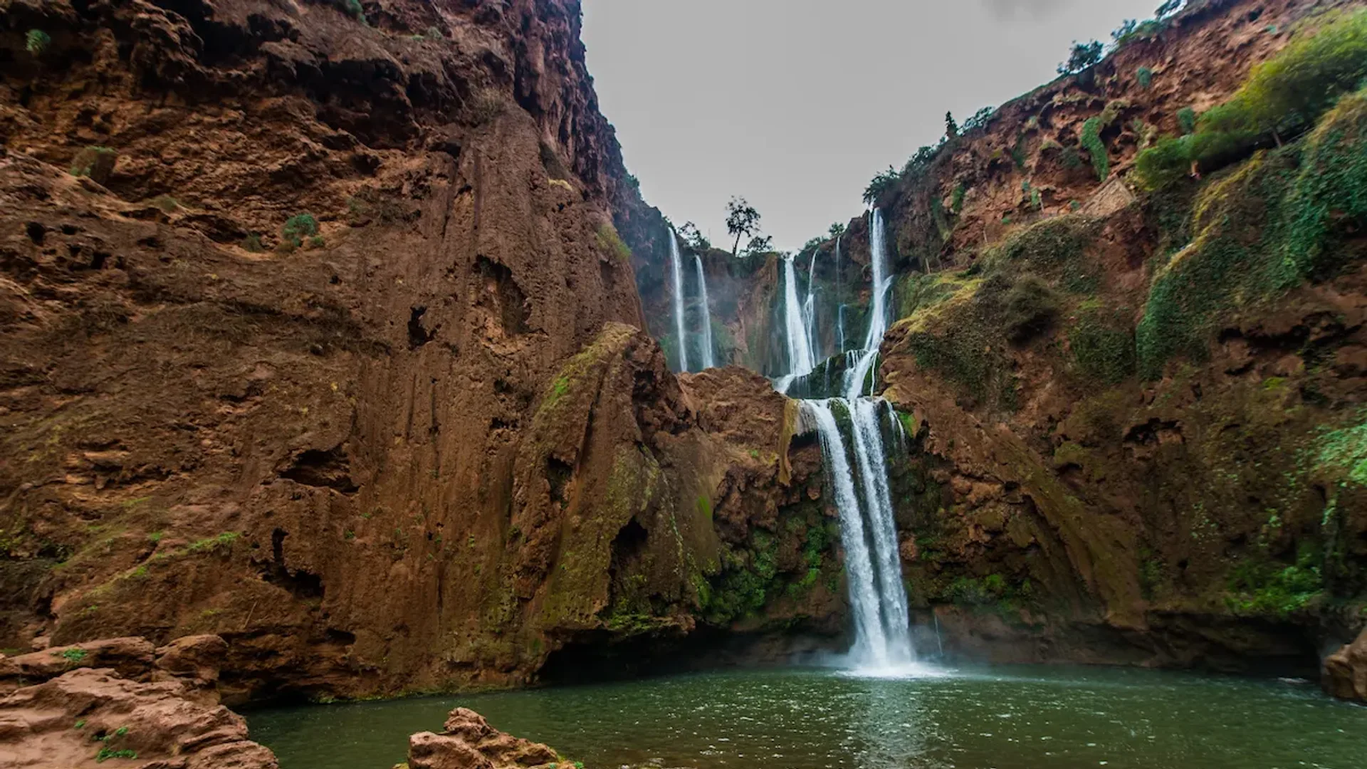 Ouzoud Falls plunging past olive groves with a rainbow in the spray and small boats at the base